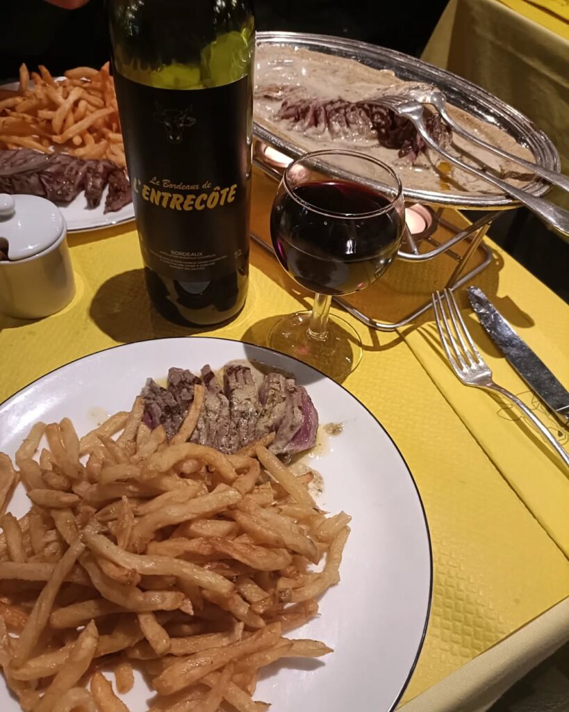 A rustic table with a bottle of Bordeaux wine, a plate of oysters, and a view of rolling vineyards, travel guide and weed laws.